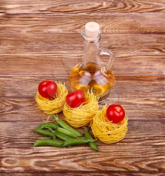 Pasta on the wooden background with tomato, lettuce pepper, olive oil and pepper.top view