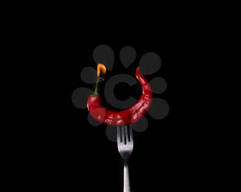 Fork impale to red hot chili on black background.