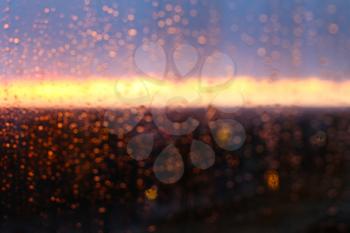 Water drops on a window glass after the rain. The sky with clouds and sun on background. Street Bokeh Lights Out Of Focus. Autumn Abstract Backdrop