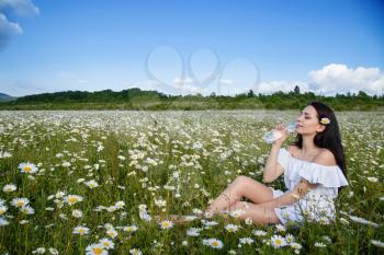Beautiful woman on a flower granden enjoying her time outdoors. pretty girl relaxing outdoor, having fun, holding plant, drinking water from a small bottle