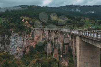 The Durdevica concrete arch bridge. Cars driving and people riding on zip-line. Tara River canyon, Montenegro.