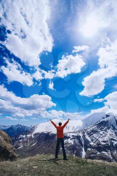 Man on top of mountain. Conceptual scene.  Young man with backpack standing with raised hands on top of a mountain and enjoying valley view