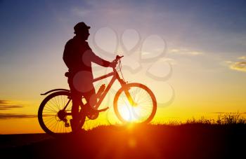 Silhouette of sports person cycling on the field on the beautiful sunset