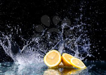 Sliced lemon in the water on black background. Fresh lemons with water splash. Dynamics of a liquid, juicy appetizing lemon and glass with splashed out water on a dark surface of a table