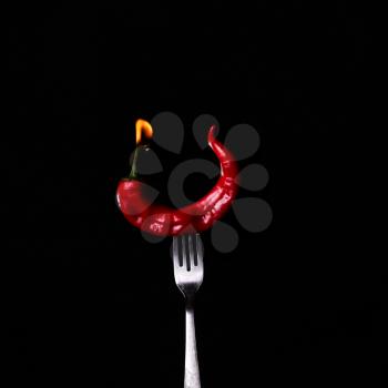 Fork impale to red hot chili on black background. 