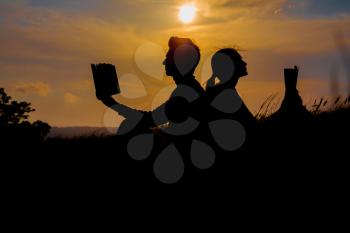 Man and woman reading in the park against sunset. Silhouette of couple reading book at sky sunset . warm tone and soft focus. Concept of love