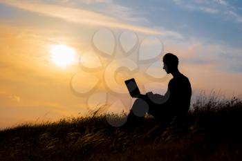 silhouette of happy business man with laptop working on the field at sunset time