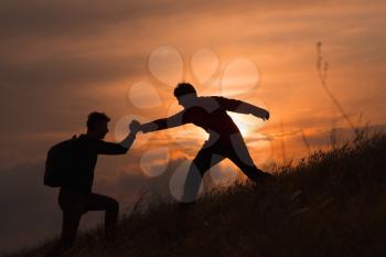 Teamwork couple hiking help each other trust assistance silhouette in mountains, sunset. Teamwork of two men hiker helping each other on top of mountain climbing team, beautiful sunset landscape.Sport