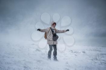 Wintery scene of shivering man in snowstorm or ice storm. Man walking in the snowstorm in the mountains