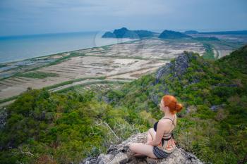 Active healthy lifestyle concept. Happy female hiker sitting on a cliff in relax pose and feeling free. Khao Daeng View Point, Thailand