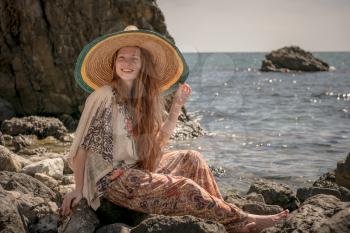 Beautiful boho styled model wearing white top and sombrero posing on the beach in sunlight