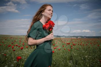 Beautiful young red-haired girl with freckles on a beautiful poppy field.
