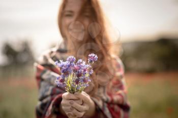 A beautiful girl enjoys the smell of a bouquet of cornflowers. Warm ethnic plaid, sunset. Beautiful red-haired young lady with freckles