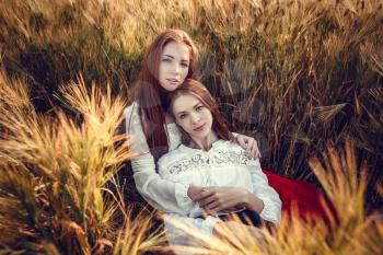 Two young women are looking forward tothe sunset. Best friends. Two young red-haired women in a wheat field