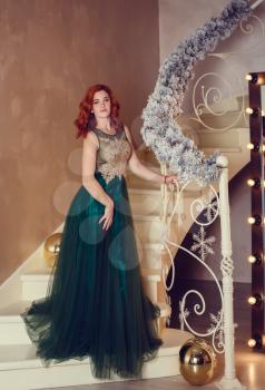 Beautiful woman in luxurious dress has found a gift under the Christmas tree. The concept of exquisite celebration of the New Year