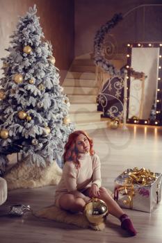 Happy young lady with curlu hair gifts by the fireplace near the Christmas tree. New year concept.
