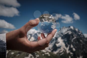 Concept and idea of travel. snow peaks of the alps seen through a glass sphere hold by a hand