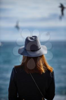 Girl looking at the calm sea on the with wind in her hair and seagulls on the background. Autumn in the Hat