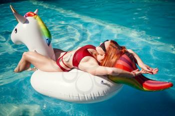 Enjoying suntan and vacation. Colorful portrait of pretty young woman in red swimsuit lying near swimming pool.