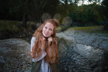 Red-Haired Woman at the Beach by the Lake in Fall Clothing. Young woman spending time by the lake in autumn.