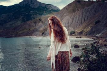 Beautiful boho styled model wearing white crochet swimsuit posing on the beach in sunlight. Red-haired girl with freckles. Crimea, Fox bay, Koktebel