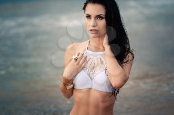 fashion photo of beautiful tanned woman with black hair in elegant white bikini relaxing on tropical island with perfect beach.