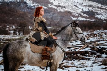 Beautiful girl on horse and with red hair in armor. Woman is a Viking. Fantasy