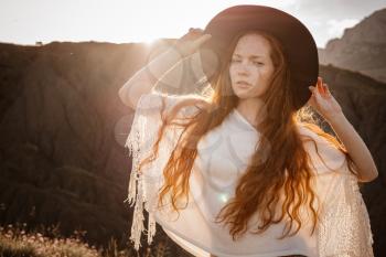 Beautiful hippie young beautiful woman with red hair dressed in boho style. Beautiful movie series at sunset. The idea of freedom