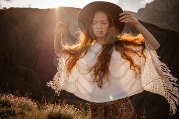Beautiful hippie young beautiful woman with red hair dressed in boho style. Beautiful movie series at sunset. The idea of freedom