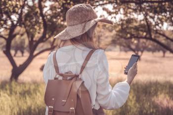 woman traveler with backpack and hat walking in amazing forest, wanderlust travel concept, atmospheric moment. earth day. use smartphone to find the way, map