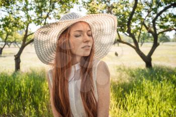Girl in the hat and dress of the garden trees. red-haired young woman with freckles on vacation