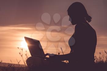 silhouette of a girl with laptop on sunset or sunrise background. Freedom at work