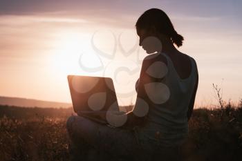 silhouette of a girl with laptop on sunset or sunrise background. Freedom at work