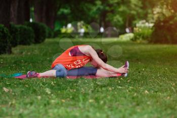 Young beautiful woman meditates on a summer day in the park. Idea and concept of calm in a busy city and a healthy lifestyle, stretching and preparing for a run in the park