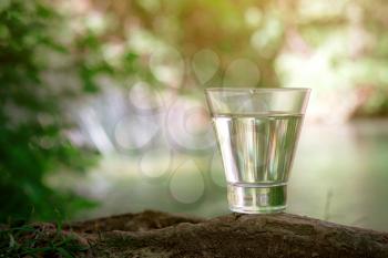 A glass of clean water, on the nature in the forest and river. Concept of a healthy lifestyle and environmental friendliness