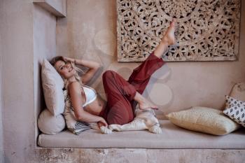 Beautiful sexy woman blonde hair east style arabic morocco furniture glamour model pose fashion clothes. room in Moroccan style fashion harem.
