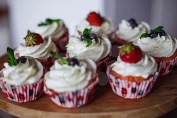 Tasty muffins decorated with red and blue berries and mint leaf. Homemade vanilla muffins with strawberry and blackberry
