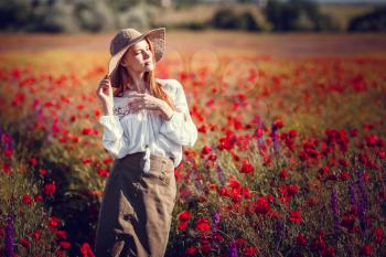Young beautiful woman walking and dancing through a poppy field, summer outdoor. Toned.