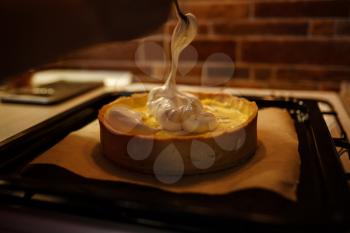 Lemon meringue pie on cutting board on brown wooden background. Preparation of lemon tart.