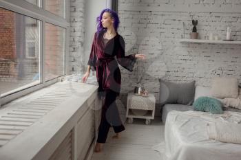 Beautiful young woman in chic velvet dark purple pajamas posing in her bedroom