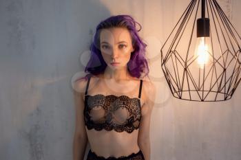 Beautiful young elegant dancer posing near an unusual lamp in her room. Delicate black lace underwear and purple hair