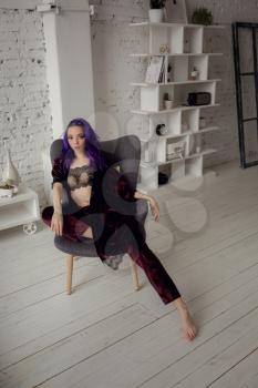 Beautiful young woman in chic velvet dark purple pajamas posing in her bedroom