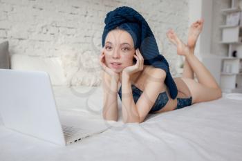 Portrait of nice cute lovely attractive winsome delicate fit slim thin girl wearing blue lingerie lying on bed linen sheets with laptop in white light room house indoors