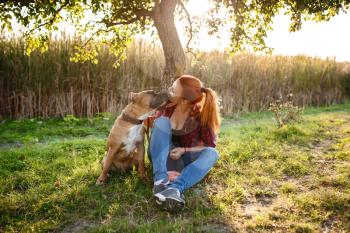 redhair jouful young woman caressing their dog, wearing sport clothing, enjoying their time and vacation in sunny park