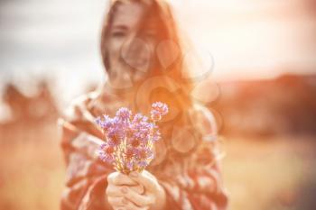 A beautiful girl enjoys the smell of a bouquet of cornflowers. Warm ethnic plaid, sunset. Beautiful red-haired young lady with freckles