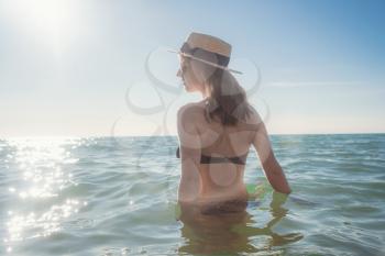 Beautiful woman having a fun while swimming in the sea. Beautiful romantic lady in a hat resting at sunset