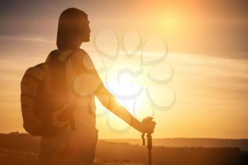 Silhouette hiker woman tracking with backpack and trekking pole, sunset orange sky on the background