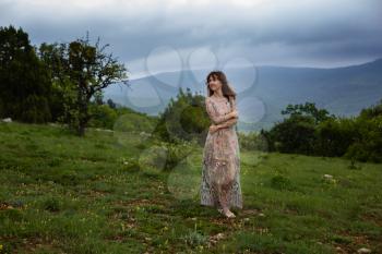 Young happy woman in long dress on the mountainside. Girl on the nature on blue sky background. Fashion photo