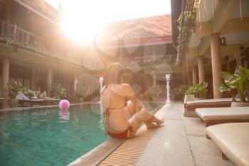 Vacation lifestyle scene of young woman sitting in swimming pool. Weekend and holiday lifestyle concept. soft light at sunset in a hotel in traditional Thai style, rest in an exotic