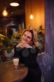 Smiling woman in a good mood with cup of coffee sitting in cafe. dark interior, evening gatherings in a cafe